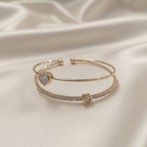 دستبند النگویی زنانه مجلسی رنگ طلایی با طراحی باز دو لاین، یک لاین ساده و یک لاین تمام نگین همراه با دو نگین درشت قلبی شکل