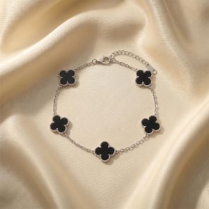 دستبند طرح ون کلیف نقره ای قرار گرفته روی پارچه ساتن با پنج پلاک شبدر چهار برگ که داخل آن‌ها مشکی است و حاشیه نقطه‌کوب شده دارند.