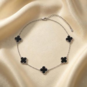 گردنبند طرح ون کلیف پنج گل نقره‌ای قرار گرفته روی پارچه ساتن روشن با پنج پلاک به شکل شبدر چهار برگ که داخل آن‌ها با رنگ مشکی پر شده و حاشیه دالبری ظریف دارند.
